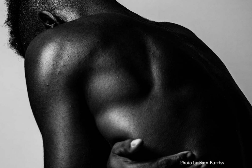 A black and white photograph of a man's bare upper body, his back turned to the camera as he clutches his side in a gesture of emotional and physical pain. The dramatic lighting highlights the tension in his muscles, symbolizing the deep emotional scars of an abandonment wound. The image evokes a sense of loneliness, loss, and inner turmoil, reflecting the silent struggles associated with emotional neglect and unresolved trauma.